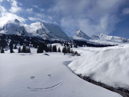 Verschneite Alp Sellamatt vor den Churfirsten im Toggenburg beim Schneeschuhwandern und ein Smiley im Schnee.